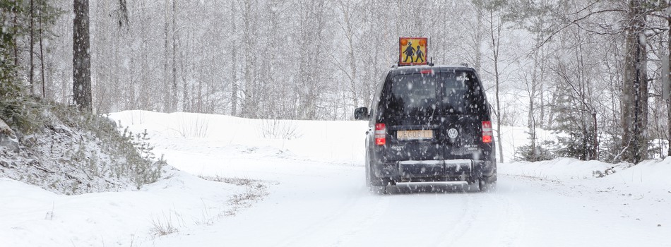 Taxi i snöväder på landsväg med skolskjutsskylt