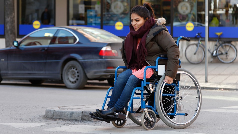 Kvinna som använder rullstol korsar en väg i en stad.