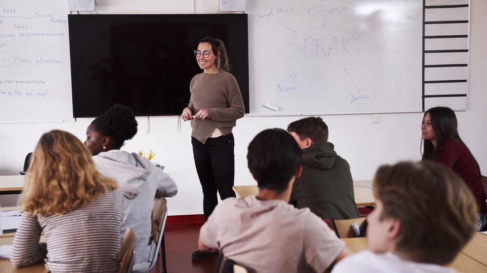 Leende kvinna står i klassrum framför elever 